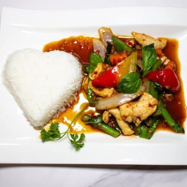 Thai West's chicken stir-fry with colorful vegetables, basil, and heart-shaped rice on a white plate.