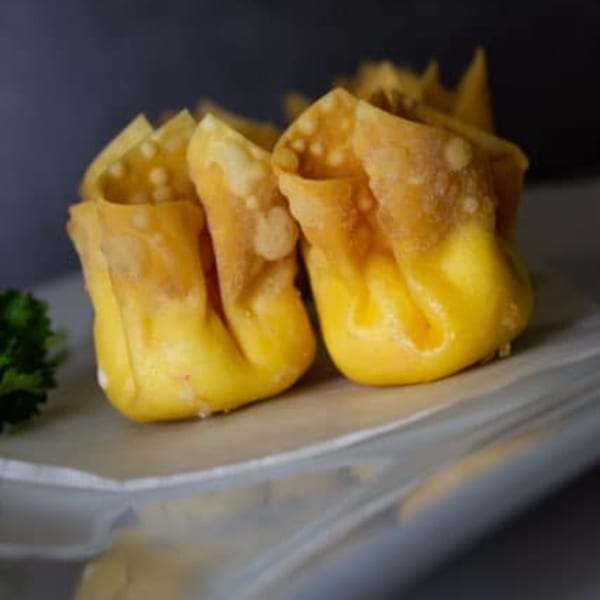 Golden-fried Thai wontons, crispy and delicious, served on a white plate with a garnish.