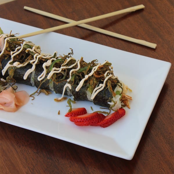 Thai West sushi roll with seaweed, sauce, pickled ginger, and strawberries on a white plate with chopsticks.