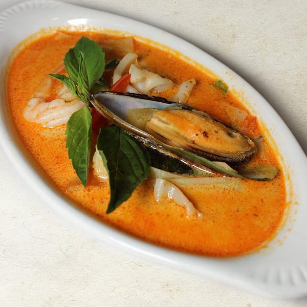 Spicy Thai red curry with mussels, shrimp, and squid, garnished with fresh basil leaves.