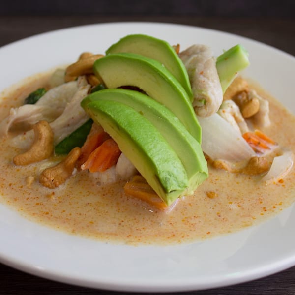 Thai West's creamy curry with chicken, cashews, carrots, and sliced avocado on a white plate.