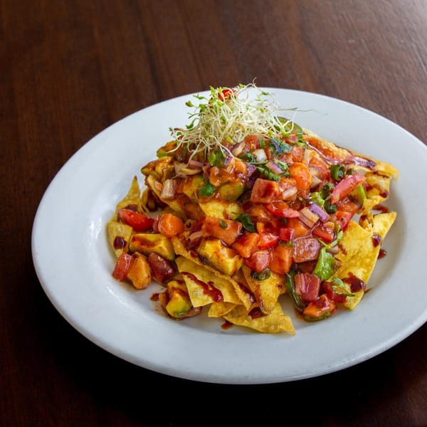 Thai nachos with diced tomatoes, avocado, red onion, and sprouts on a white plate.