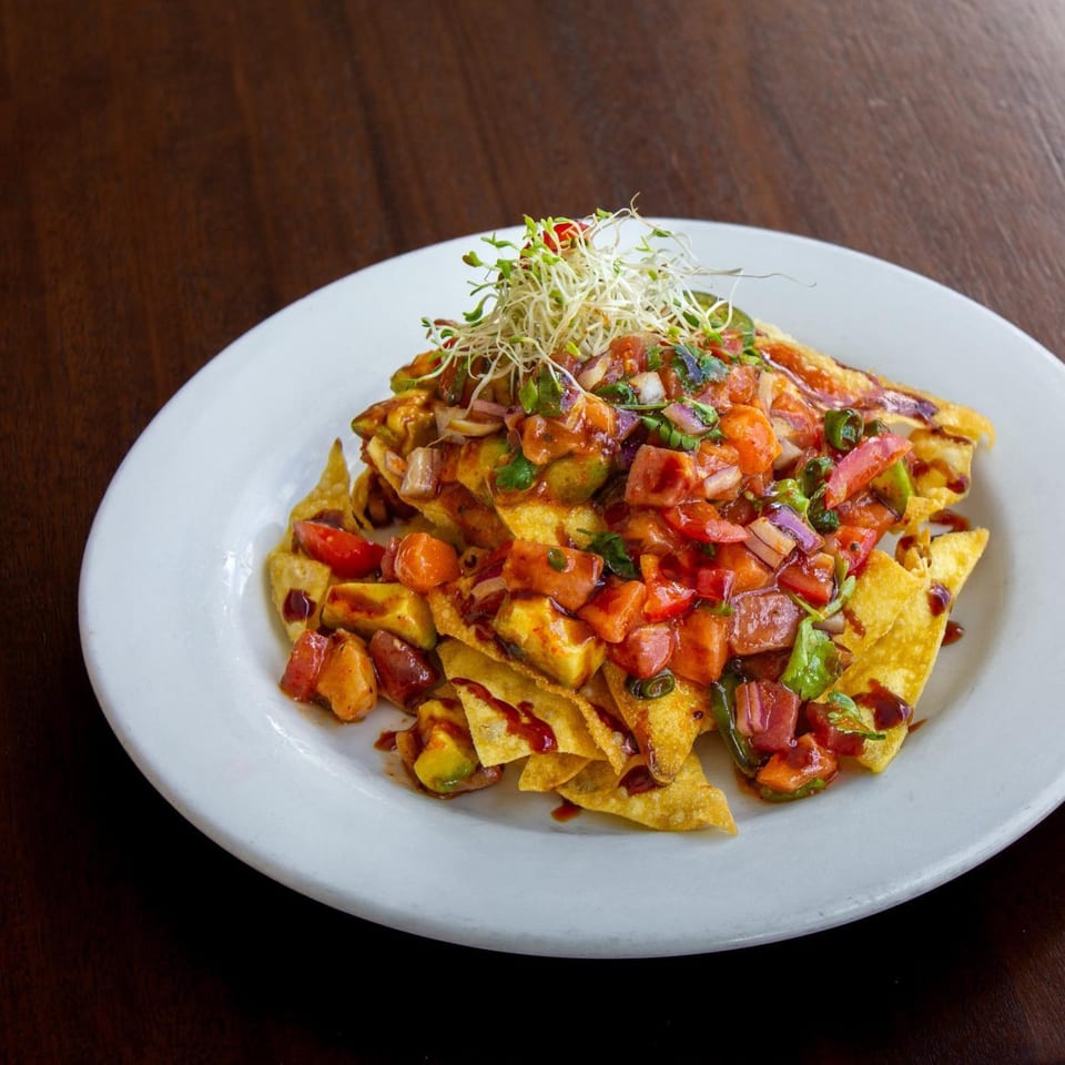 Thai nachos with diced tomatoes, avocado, red onion, and sprouts on a white plate.